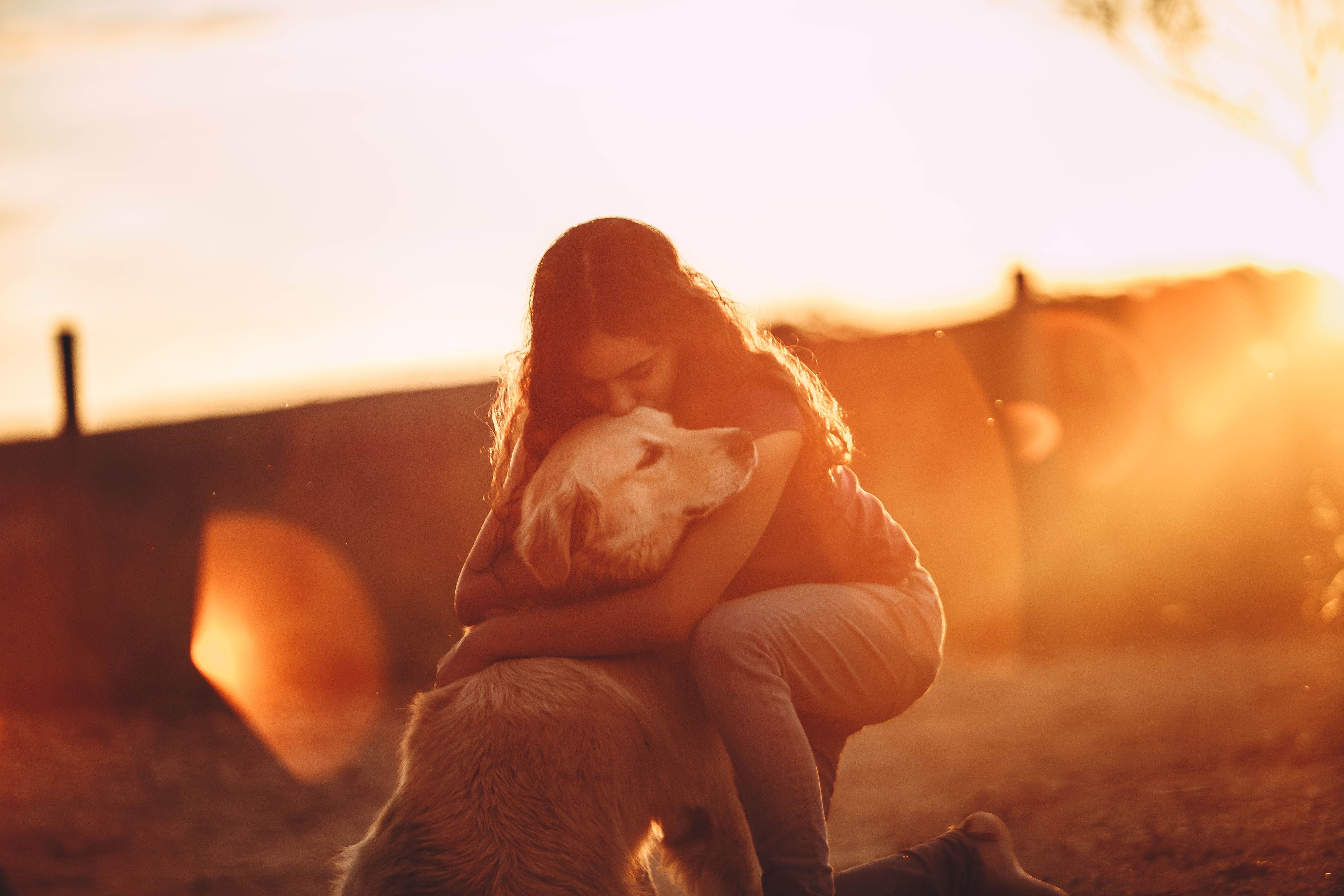 A woman holding her golden retriever close in the evening light.